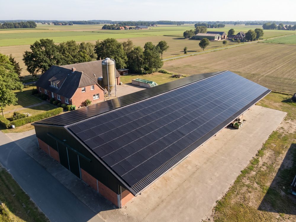 Hof mit Maschinenhalle, deren Dach mit Full-Black-Modulen belegt ist (KI-generiertes Bild)