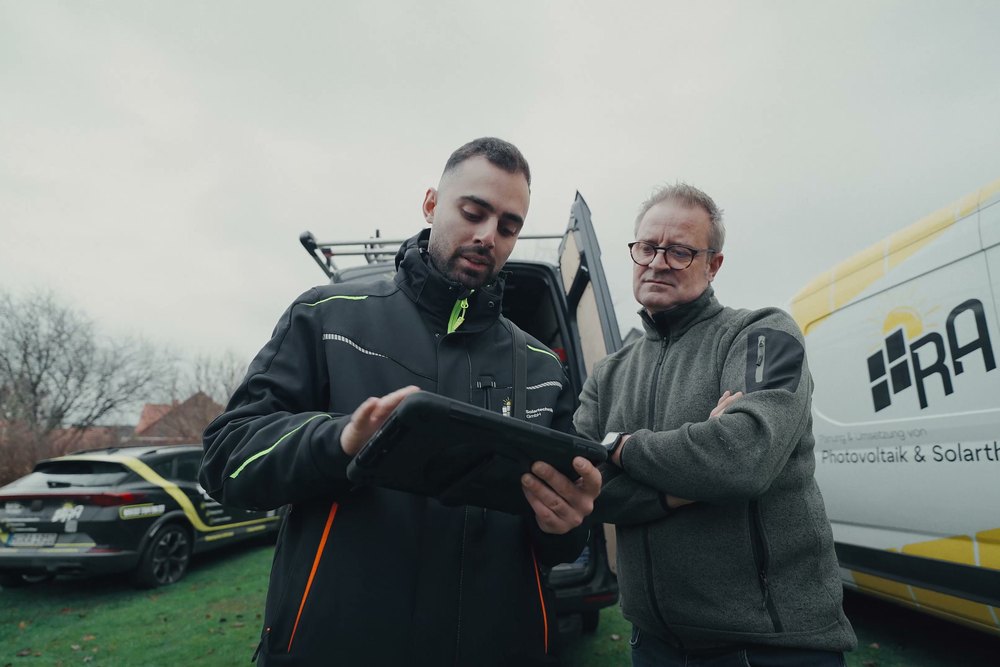 Berater von RA Solartechnik bespricht mit einem Kunden die Planung am Tablet vor dem Firmenwagen