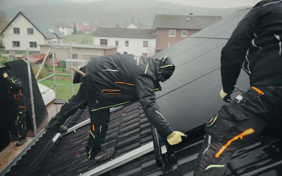 Zwei Monteure befestigen Solarmodule auf einem Ziegeldach