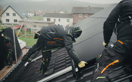 Zwei Monteure befestigen Solarmodule auf einem Ziegeldach