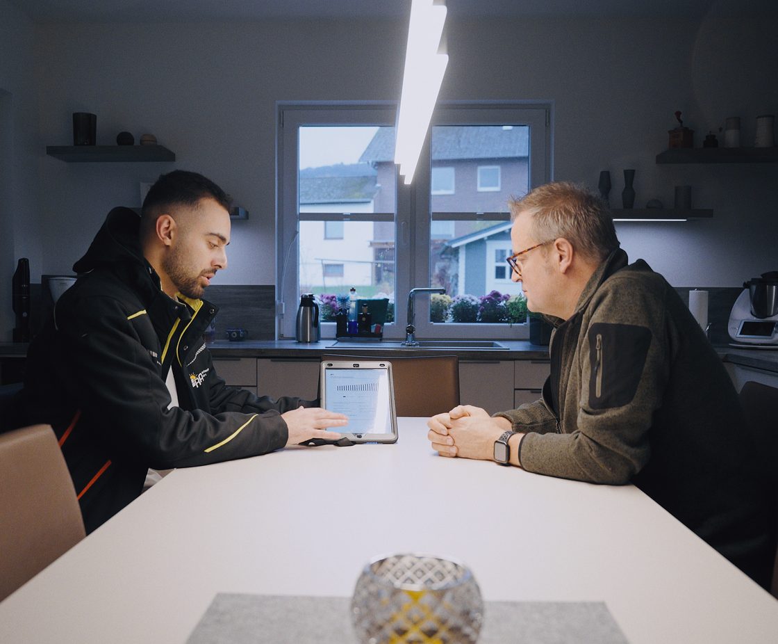 Ali Noureddine, Kundenberater bei RA Solartechnik, bespricht mit einem Kunden am Küchentisch eine Auswertung auf dem Tablet