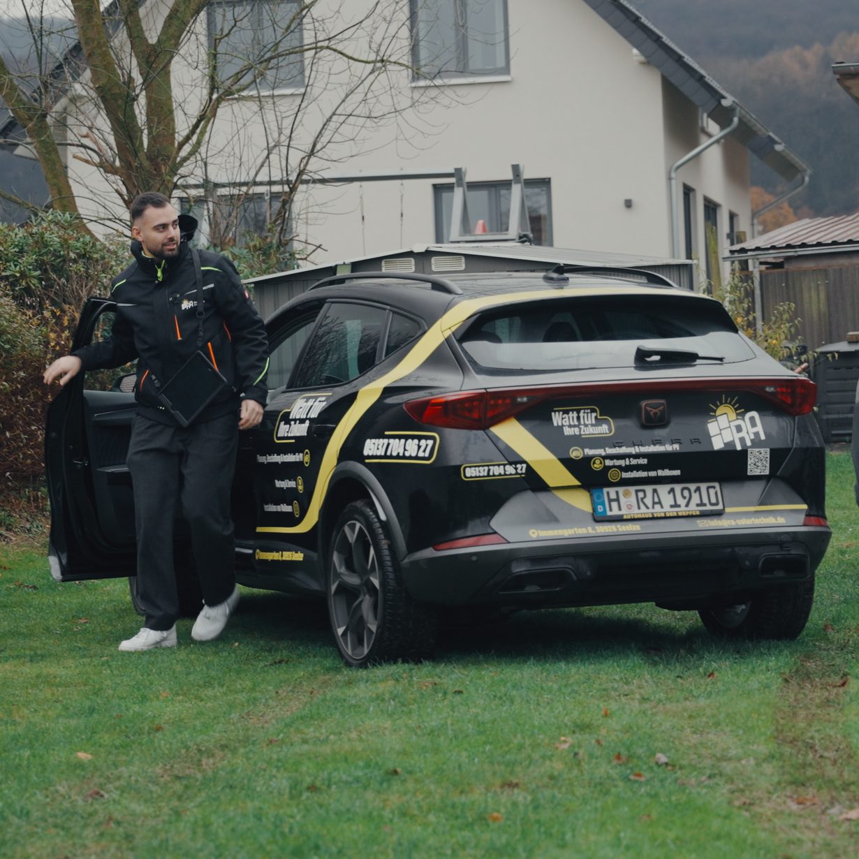 Ali Noureddine, Kundenberater bei RA Solartechnik, steht vor einem Einfamilienhaus an der offenen Tür des beschrifteten Firmenwagens von RA Solartechnik