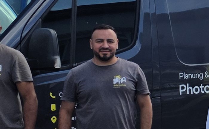 Abdelrahman Rashid, Geschäftsführer von RA Solartechnik, im grauen RA-Shirt vor dem schwarzen Firmentransporter mit RA-Beschriftung, links angeschnitten ein Kollege