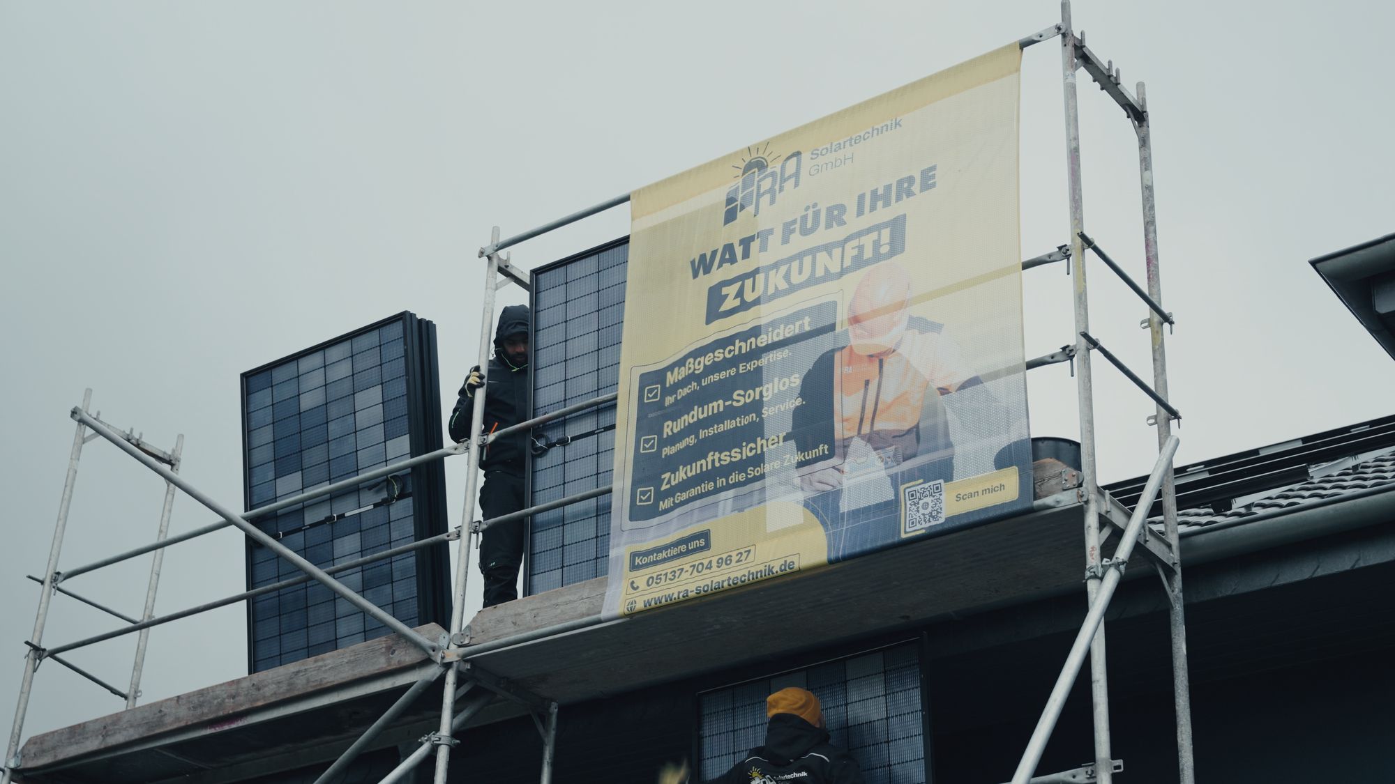 Monteur von RA Solartechnik auf dem Gerüst mit Solarmodulen, daneben das Banner „Watt für Ihre Zukunft“