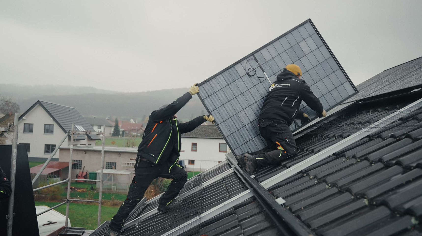 Zwei Monteure von RA Solartechnik tragen ein Solarmodul auf ein Ziegeldach