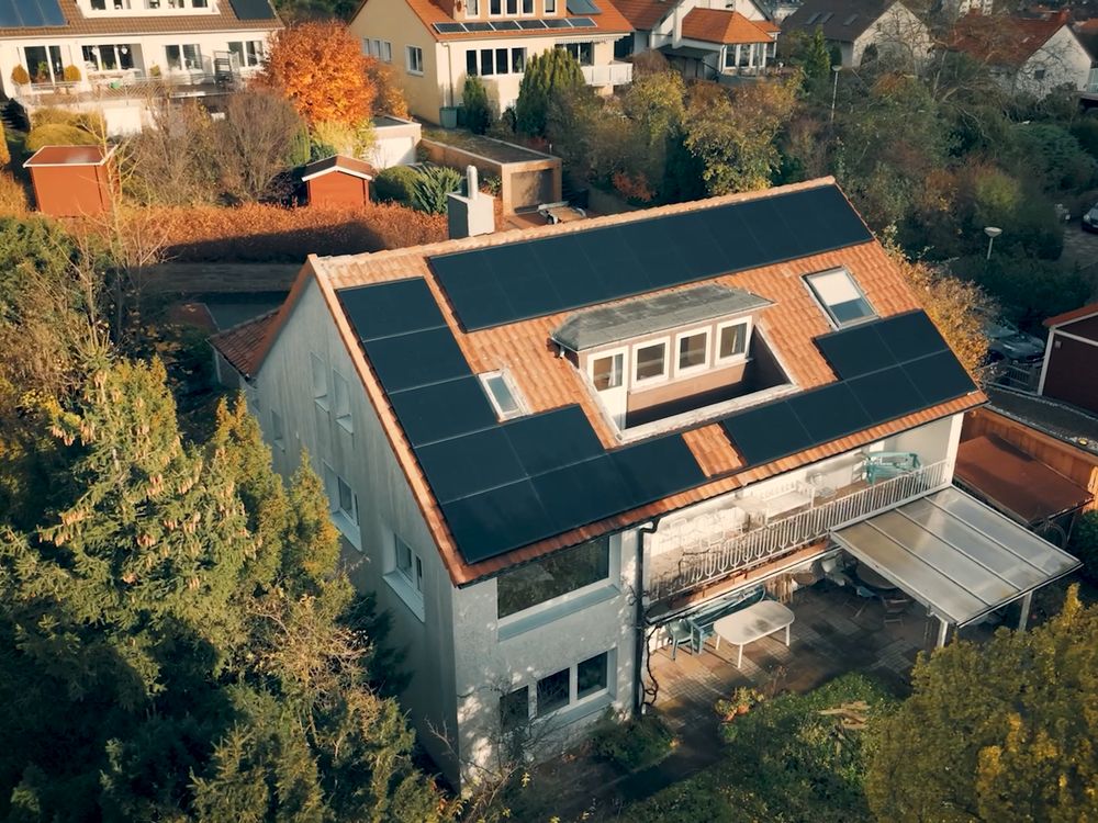 Luftaufnahme eines Einfamilienhauses mit Solarmodulen auf mehreren Dachflächen, davor der Montagewagen