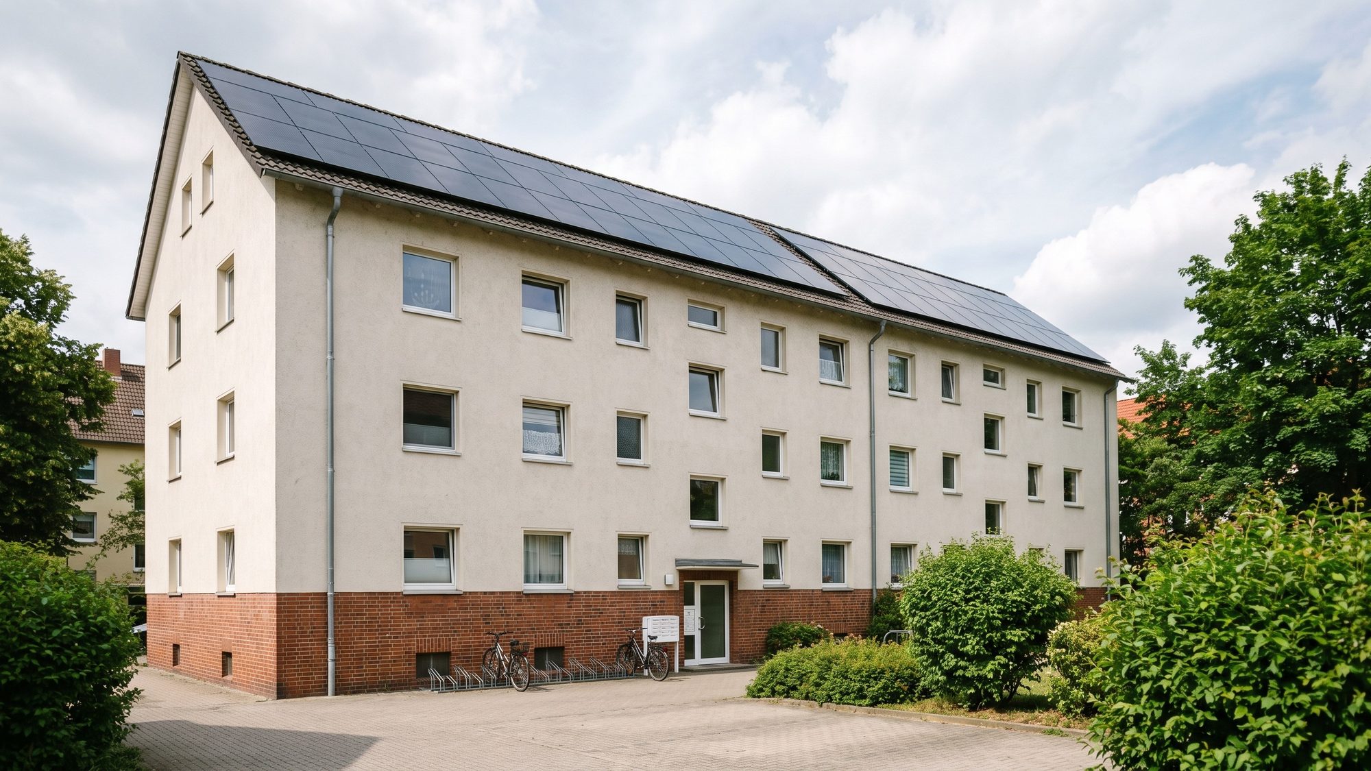 Mehrfamilienhaus mit hellem Putz aus der Hofperspektive, auf dem Dach Full-Black-Solarmodule (KI-generiertes Bild)