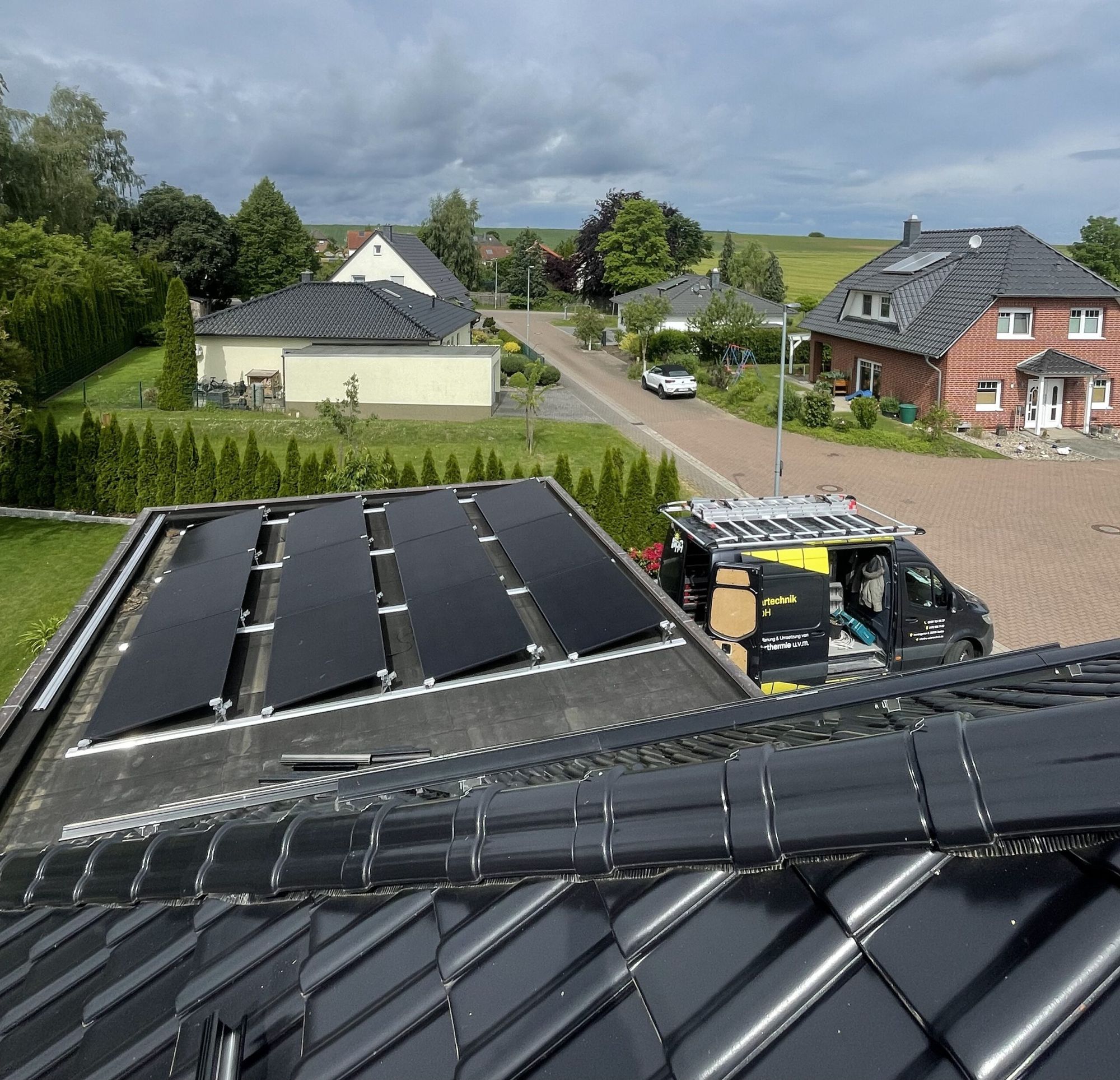 Drohnenaufnahme: Photovoltaikanlage auf einem Dach, davor der RA-Firmenwagen