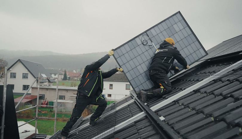 Zwei Monteure tragen ein Solarmodul über das Dach