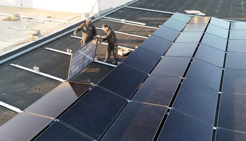 Zwei Monteure tragen ein Solarmodul über das Flachdach der Anlage in Hannover-Mittelfeld