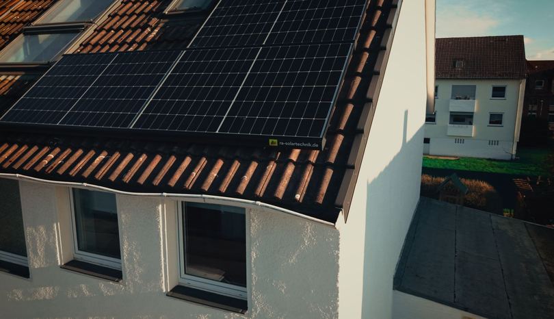 Solarmodule mit RA-Solartechnik-Aufkleber am Dachrand eines Wohnhauses