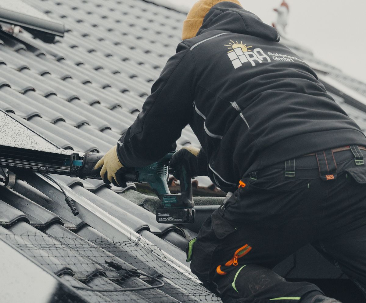 Monteur von RA Solartechnik befestigt mit dem Akkuschrauber schwarze Solarmodule auf einem Ziegeldach