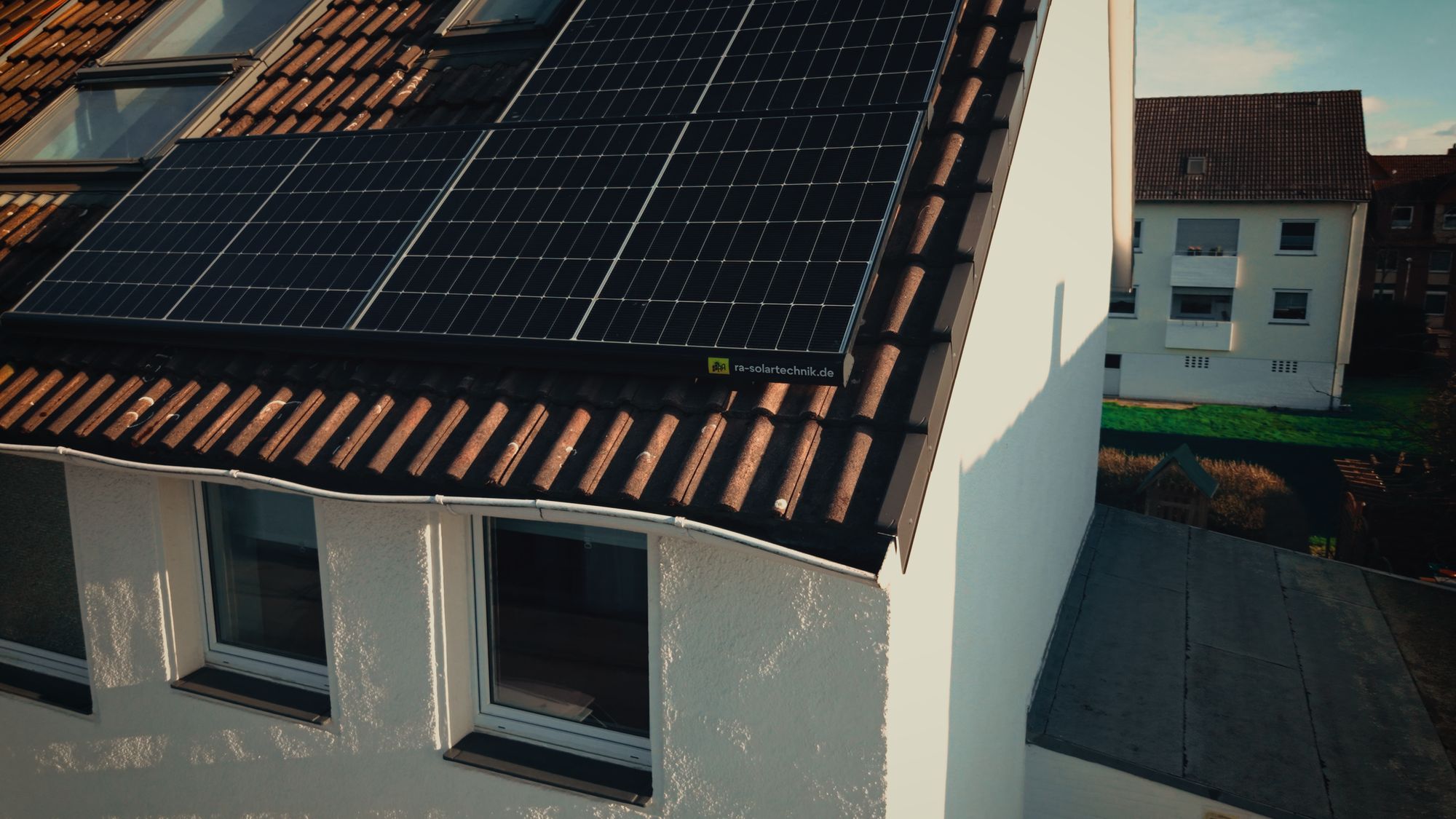 Solarmodule mit RA-Solartechnik-Aufkleber am Dachrand eines Wohnhauses