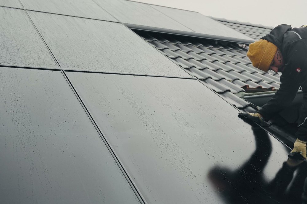 Monteur mit Arbeitshandschuhen prüft regennasse Solarmodule auf einem Ziegeldach