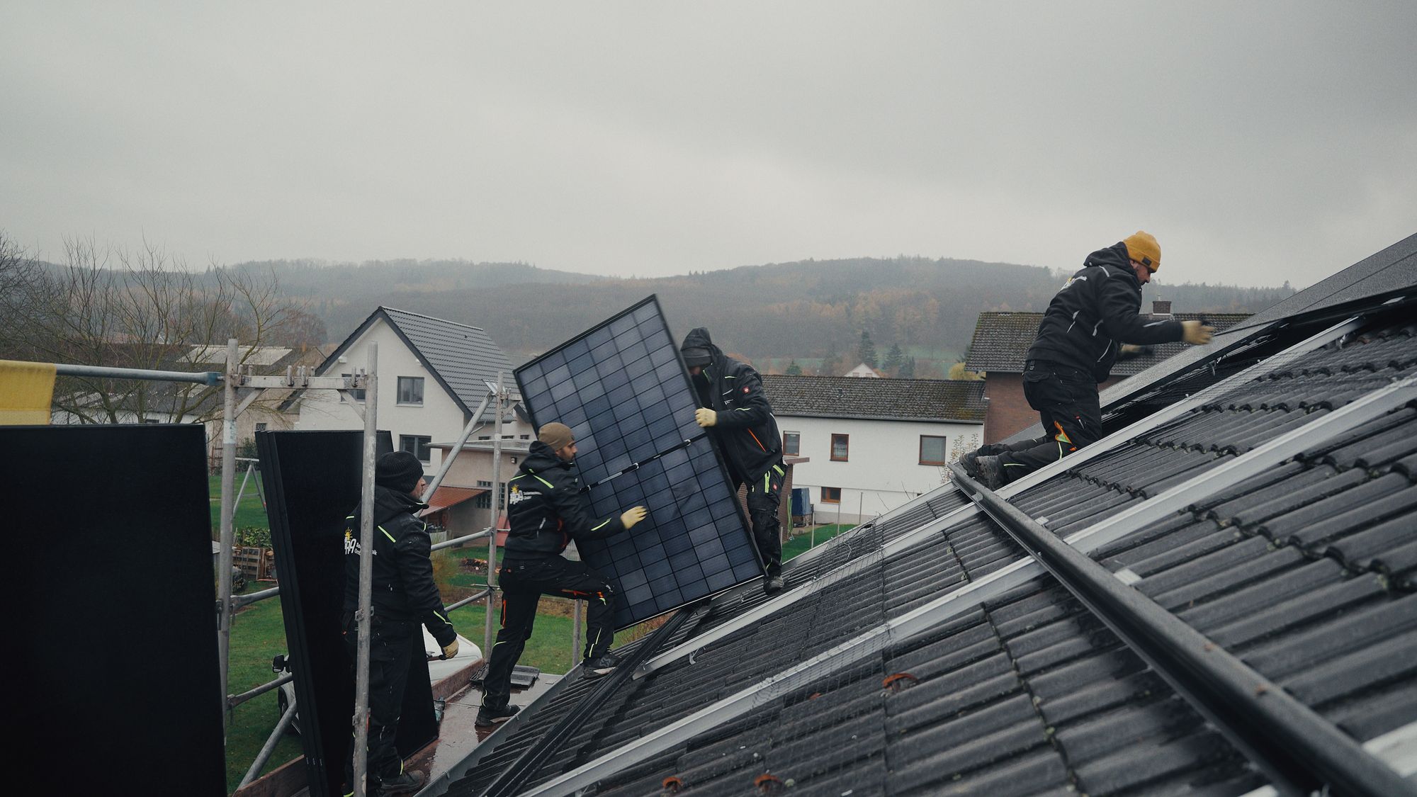 Monteure von RA Solartechnik tragen ein Full-Black-Solarmodul auf ein Dach