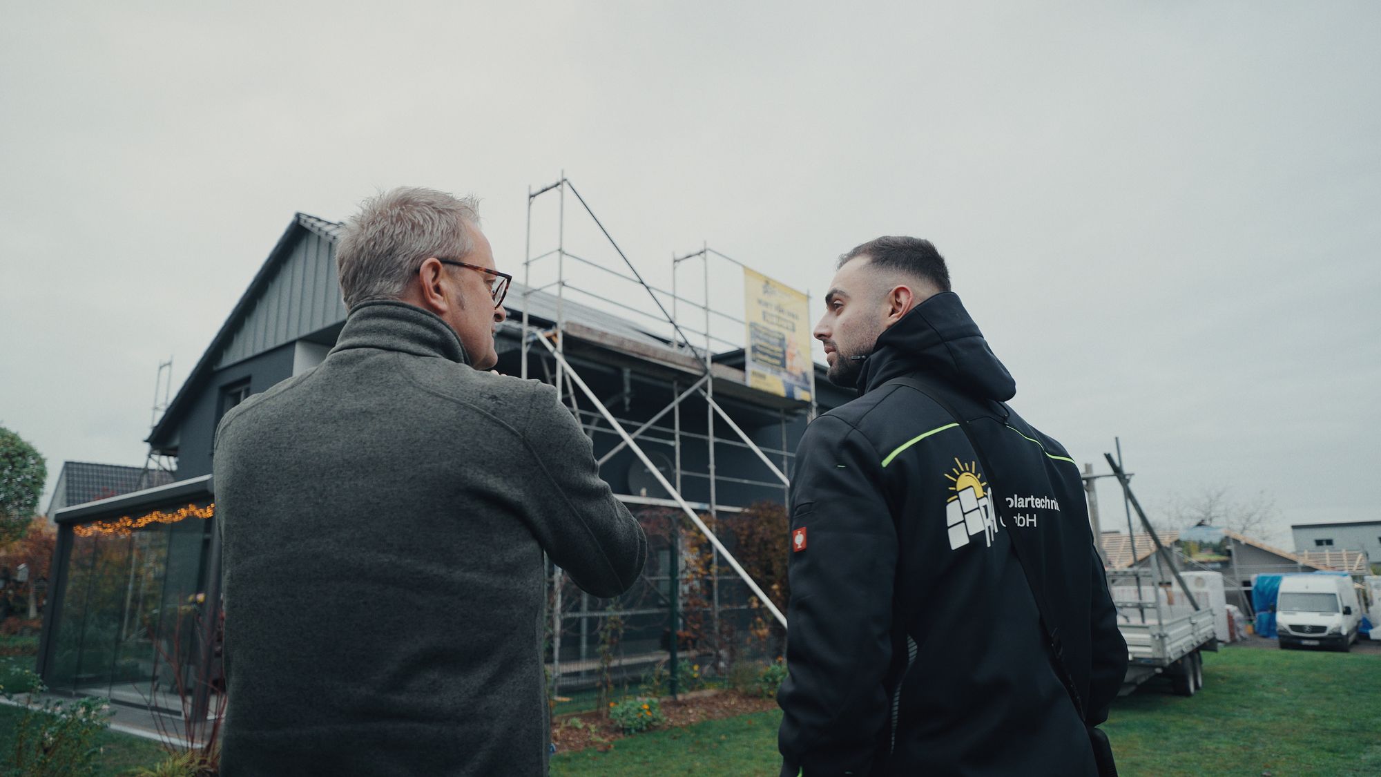 Mitarbeiter von RA Solartechnik im Gespräch mit einem Kunden vor einem eingerüsteten Haus