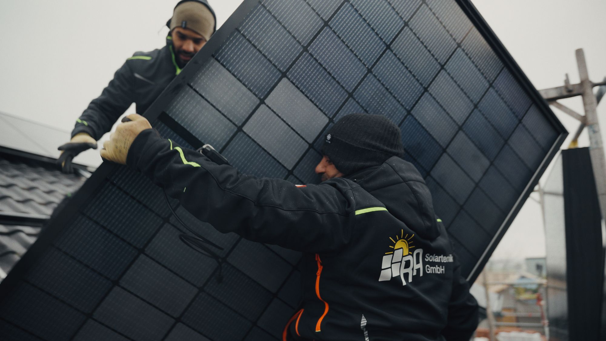 Zwei Monteure von RA Solartechnik tragen ein Full-Black-Solarmodul über das Dach